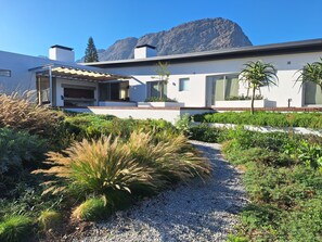 A modern house with a patio, surrounded by a well-maintained garden and a mountain in the background. - 6 on Heide (Franschhoek)