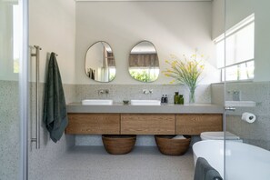 A modern bathroom with two sinks, wooden cabinets, a glass shower enclosure, and a vase with yellow flowers. - 6 on Heide (Franschhoek)