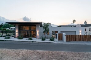 A modern two-story house with a garage, a fenced driveway, and a mountain backdrop. - 6 on Heide (Franschhoek)