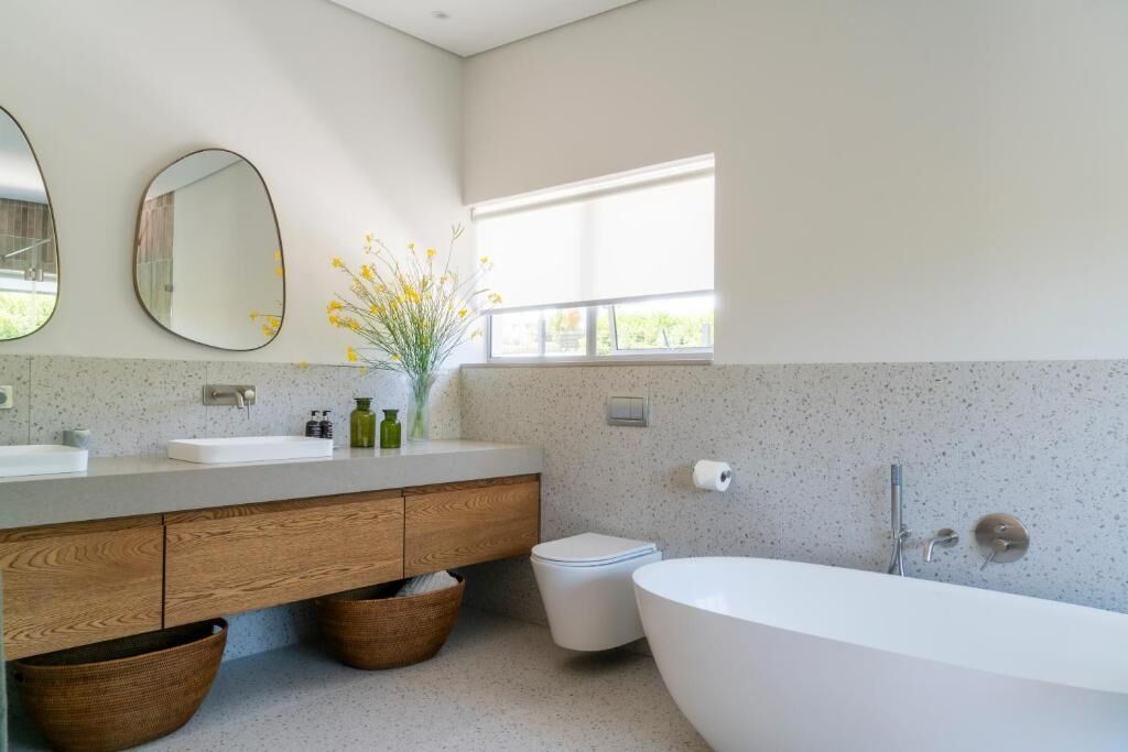 Un baño moderno con una bañera independiente, un tocador de madera, un inodoro y un ventanal que aporta luz natural.