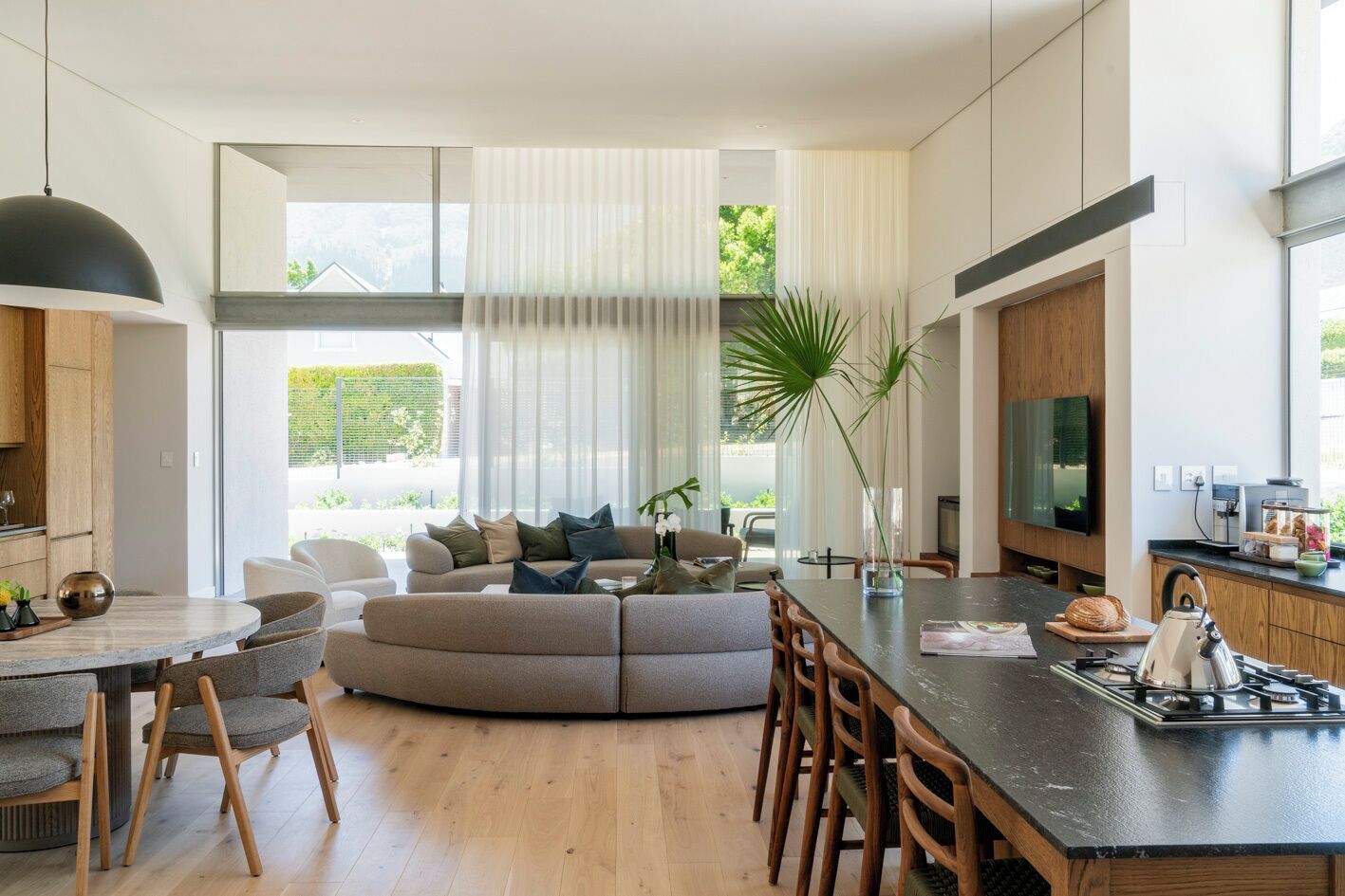 Un salon moderne avec un canapé aux lignes courbes, un coin repas doté d’une table ronde et une cuisine équipée d’une cuisinière à gaz.
