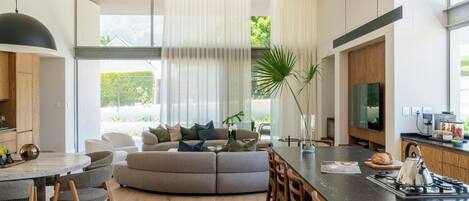 A modern living room with a curved sofa, a dining area with a round table, and a kitchen with a gas stove.