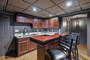 A modern kitchen with wooden cabinets, a marble countertop, and a built-in bar area. - Sand Valley Golf & ATV Lodge: Hot Tub, Bar (Nekoosa)