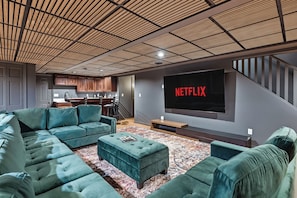 A modern living room with a large flat-screen TV mounted on the wall, a sectional sofa, and a coffee table. - Sand Valley Golf & ATV Lodge: Hot Tub, Bar (Nekoosa)
