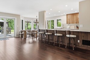 A modern kitchen with a bar area, wooden flooring, and large windows offering views of greenery. - Sand Valley Golf & ATV Lodge: Hot Tub, Bar (Nekoosa)