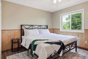 A bedroom with a bed, a nightstand, a window, and a view of trees. - Sand Valley Golf & ATV Lodge: Hot Tub, Bar (Nekoosa)