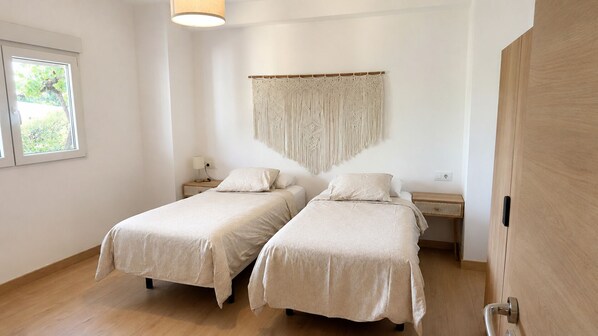 A room with two beds, a macrame wall hanging, and a wooden door.