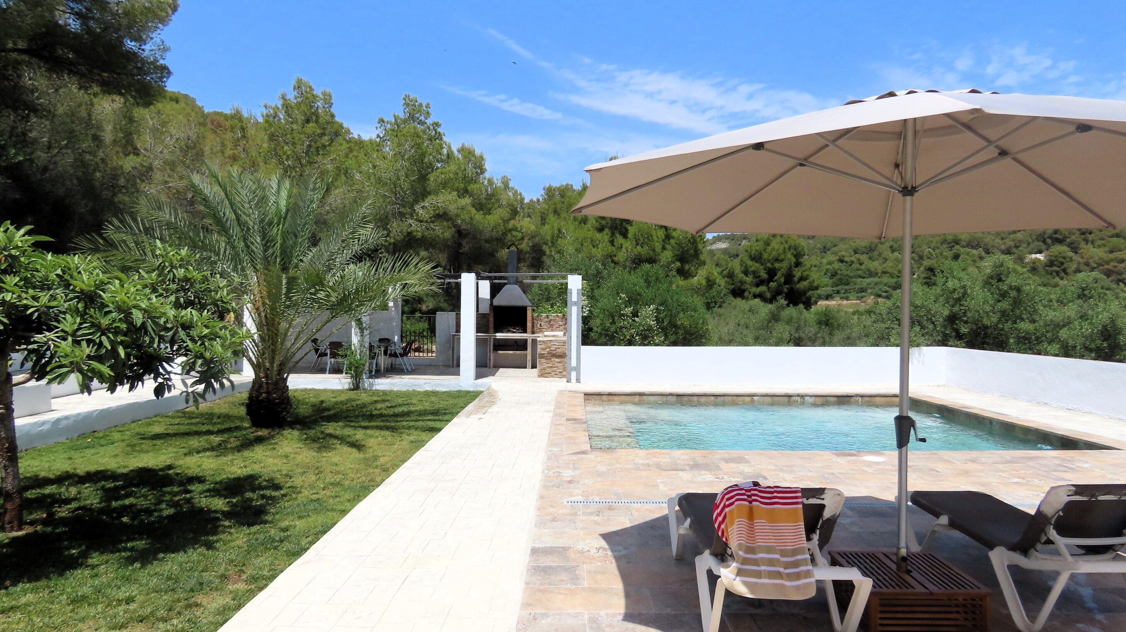 Un espace aménagé au bord de la piscine, comprenant un barbecue, des chaises longues et un parasol.