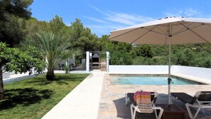 A poolside area with a barbecue grill, lounge chairs, and an umbrella.