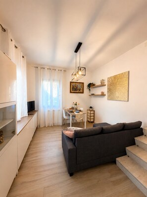 A modern living room with a sofa, a dining area with a table and chairs, and a kitchen area with cabinets and a TV. - Cozy apartment 10-minute bus ride from the heart of Venice (Venezia)