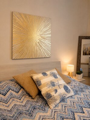 A bedroom with a bed, pillows, a wall-mounted artwork, a bedside lamp, and a nightstand with a plant. - Cozy apartment 10-minute bus ride from the heart of Venice (Venezia)