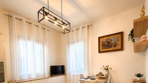 A modern living room with a grey sofa, a dining table with chairs, a TV on a cabinet, and a painting on the wall. - Cozy apartment 10-minute bus ride from the heart of Venice (Venezia)