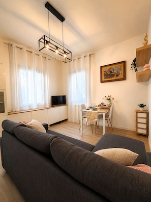 Ein modernes Wohnzimmer mit einem grauen Sofa, einem Esstisch mit Stühlen, einem Fernseher auf einer Kommode und einem Gemälde an der Wand.