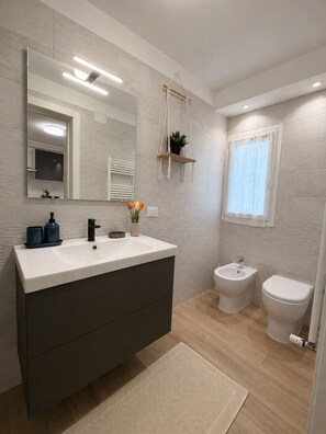 Ein modernes Badezimmer mit einem großen Spiegel, einem Waschtisch, einem Bidet und einer Toilette.