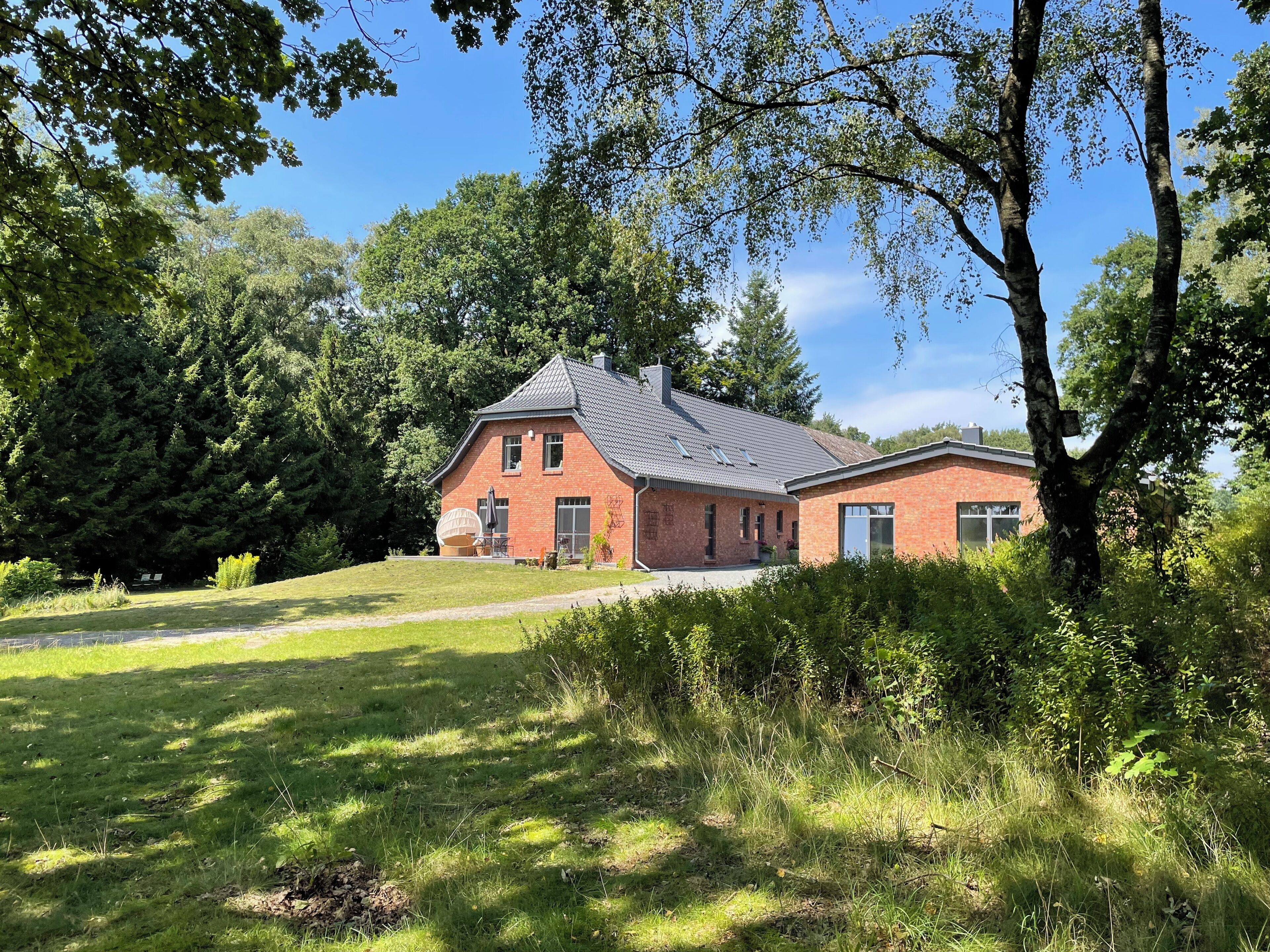 A two-story brick house with a sloped roof, surrounded by lush greenery and trees.