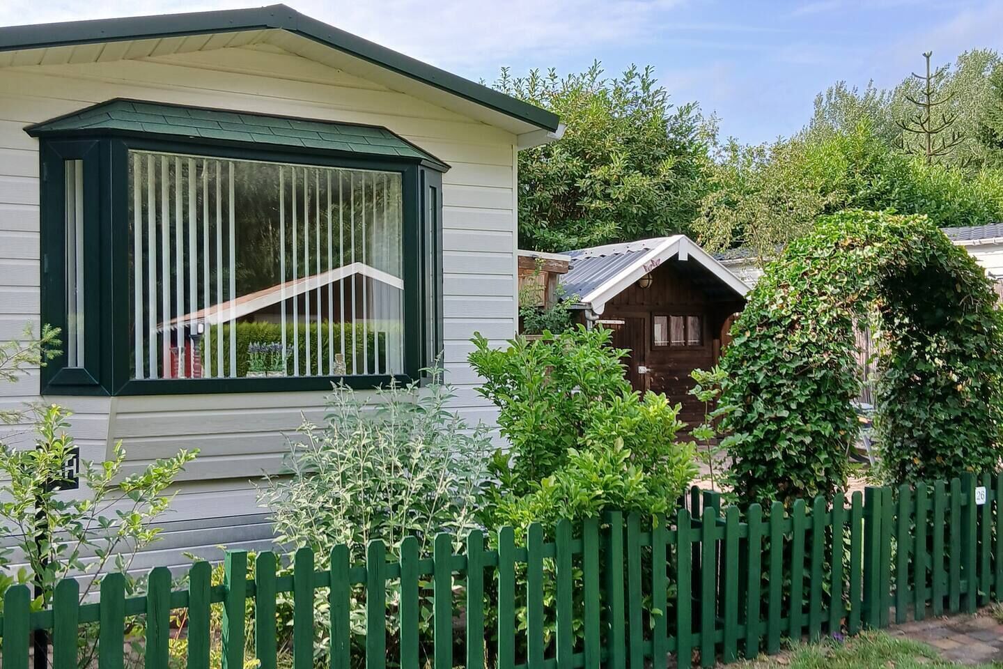A single-story house with a bay window, a wooden door, and a green picket fence.