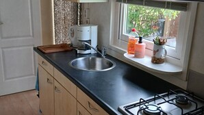 Een keuken met een spoelbak, fornuis en raam met uitzicht op een tuin.
