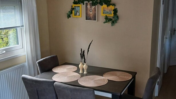 Een eetgedeelte met een tafel voor vier personen, met geweven placematen en een vaas met decoratieve takken.