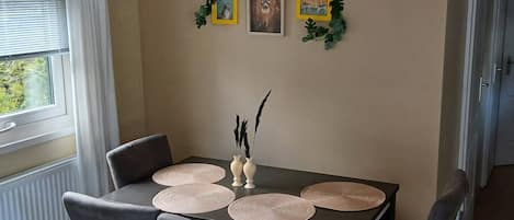 A dining area with a table set for four, featuring woven placemats and a vase with decorative branches.