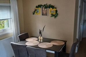 A dining area with a table set for four, featuring woven placemats and a vase with decorative branches.