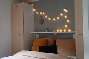 A bedroom with a bed, pillows, a shelf with decorative lights, and a heart-shaped ornament.