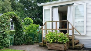 Een huis met een houten trap naar een deur, omgeven door groen en een metselpad.