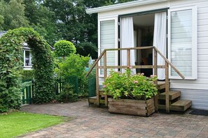 Ein Haus mit einer Holztreppe, die zu einer Tür führt, umgeben von Grünpflanzen und einem Pflasterweg.