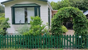 Een stacaravel met een groene picket hek, een overdekte veranda en een kleine tuin.