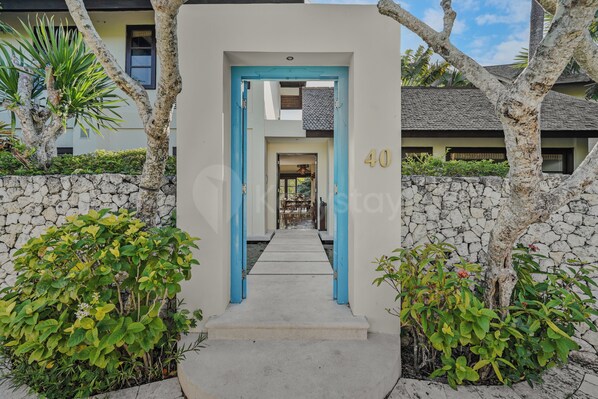 A pathway leading to a building entrance with a stone wall and tropical plants.