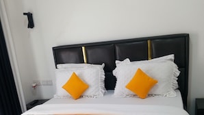 Una cama con una colcha blanca acolchada, dos almohadas con borde festoneado y un tejido naranja decorativo.