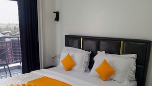 Habitación de hotel con cama, mesita de noche, ventana con cortinas y vista a la ciudad.