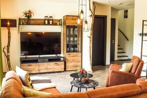 A modern living room with a flat-screen TV, wooden furniture, a round coffee table, and a staircase in the background. - SEEside13. Lake view. Sauna. Front Row at Diemelsee (Diemelsee)