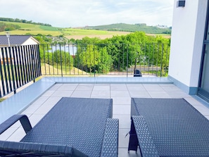 A balcony with two lounge chairs, a view of a lake, and a hilly landscape in the background. - SEEside13. Lake view. Sauna. Front Row at Diemelsee (Diemelsee)
