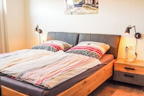 A bed with a striped bedspread, two pillows, a headboard, bedside tables with lamps, and a wall-mounted picture. - SEEside13. Lake view. Sauna. Front Row at Diemelsee (Diemelsee)