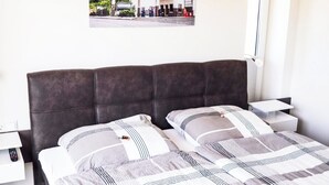 A bedroom with a large bed, two bedside tables, a nightstand, a lamp, and a poster on the wall. - SEEside13. Lake view. Sauna. Front Row at Diemelsee (Diemelsee)