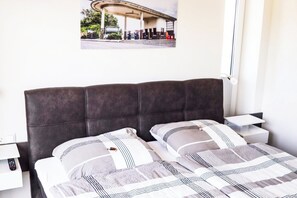 A bedroom with a large bed, two bedside tables, a nightstand, a lamp, and a poster on the wall. - SEEside13. Lake view. Sauna. Front Row at Diemelsee (Diemelsee)