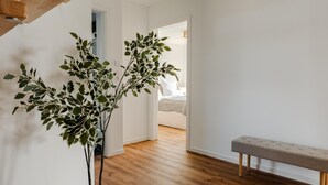 Un pasillo con un banco de madera, una planta en maceta y una cama al fondo.