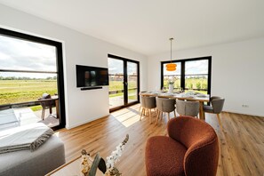 Una zona de menjador moderna amb una taula de fusta, cadires grises i un televisor penjat a la paret.
