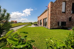 A modern brick building with a well-maintained lawn and a paved pathway leading to the entrance. - Hildes Huuske | Right on the Water - Outdoor Sauna (Greetsiel)