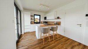 Una cocina moderna con muebles blancos, encimera de madera y dos taburetes de bar.