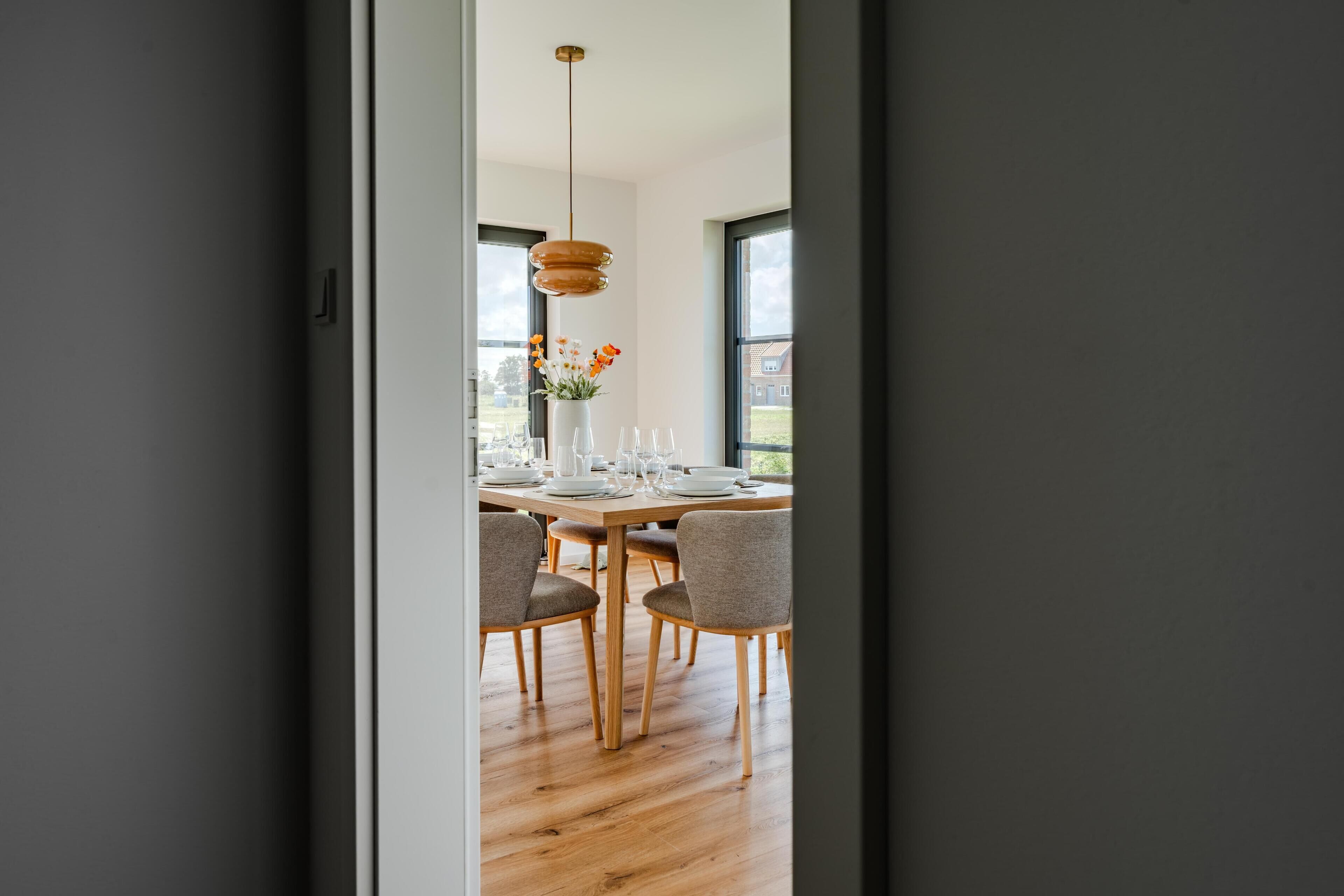 A modern dining area with a wooden table set for four, surrounded by chairs, and a hanging pendant light above.