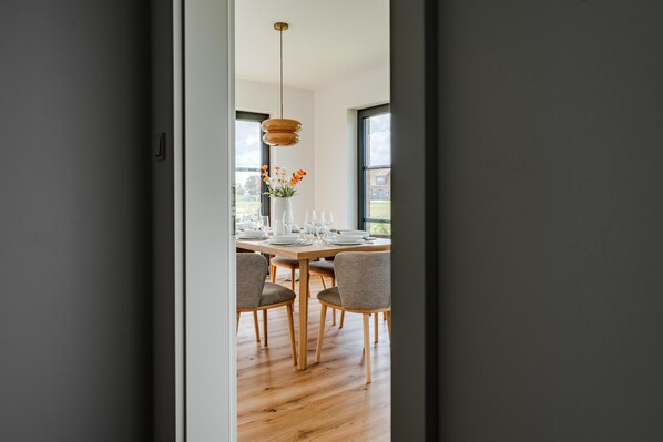 A modern dining area with a wooden table set for four, surrounded by chairs, and a hanging pendant light above.