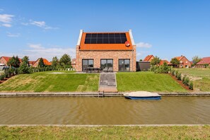 Una casa moderna con techo solar, una lancha varada cerca del agua y un césped bien cuidado.