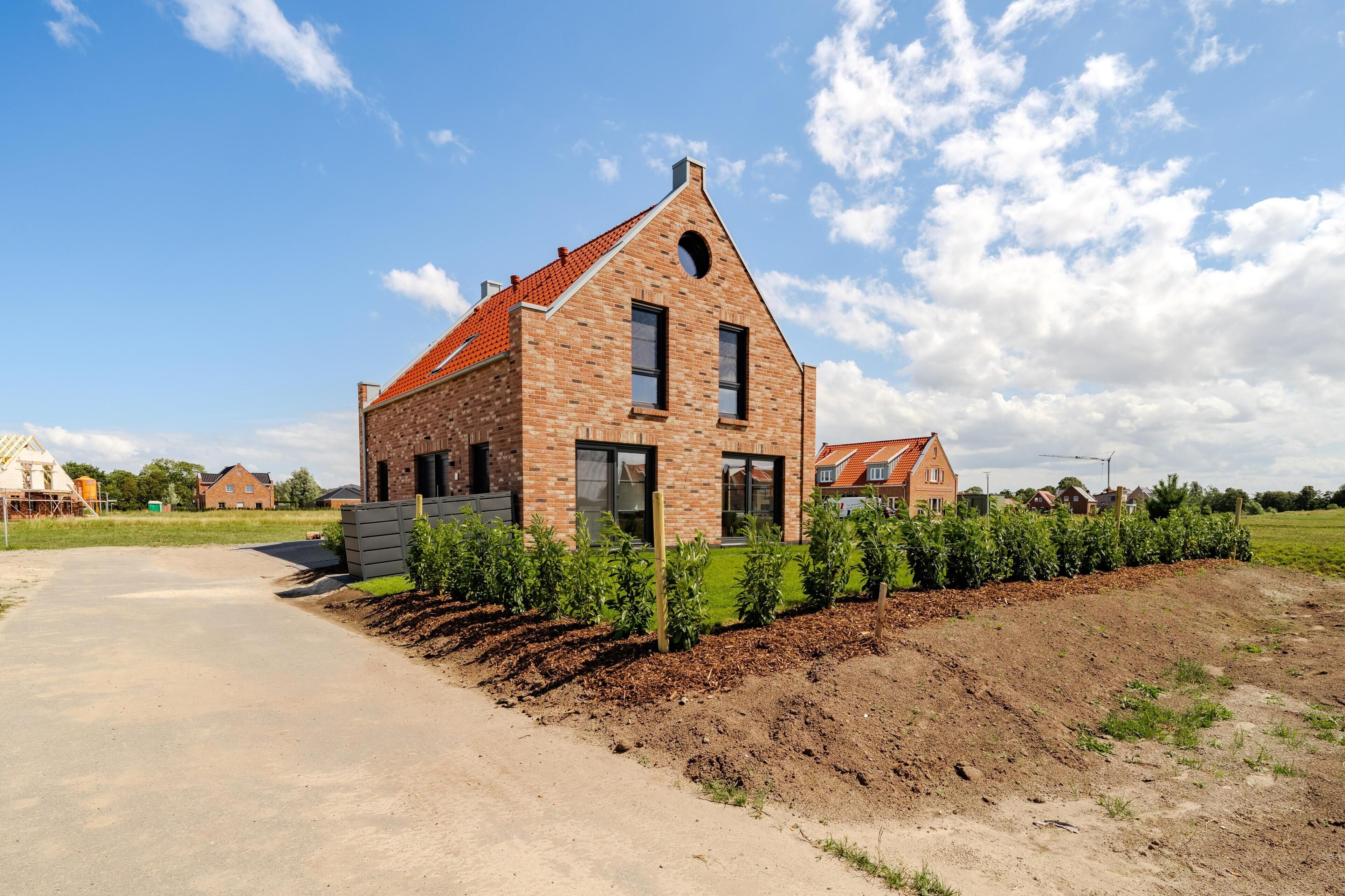 A modern brick house with a sloped roof, a paved driveway, and a garden with young plants.