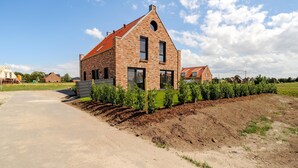 Una casa moderna de ladrillo con techo inclinado, entrada pavimentada y jardín con plantas jóvenes.
