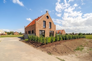 A modern brick house with a sloped roof, a paved driveway, and a garden with young plants. - Hildes Huuske | Right on the Water - Outdoor Sauna (Greetsiel)