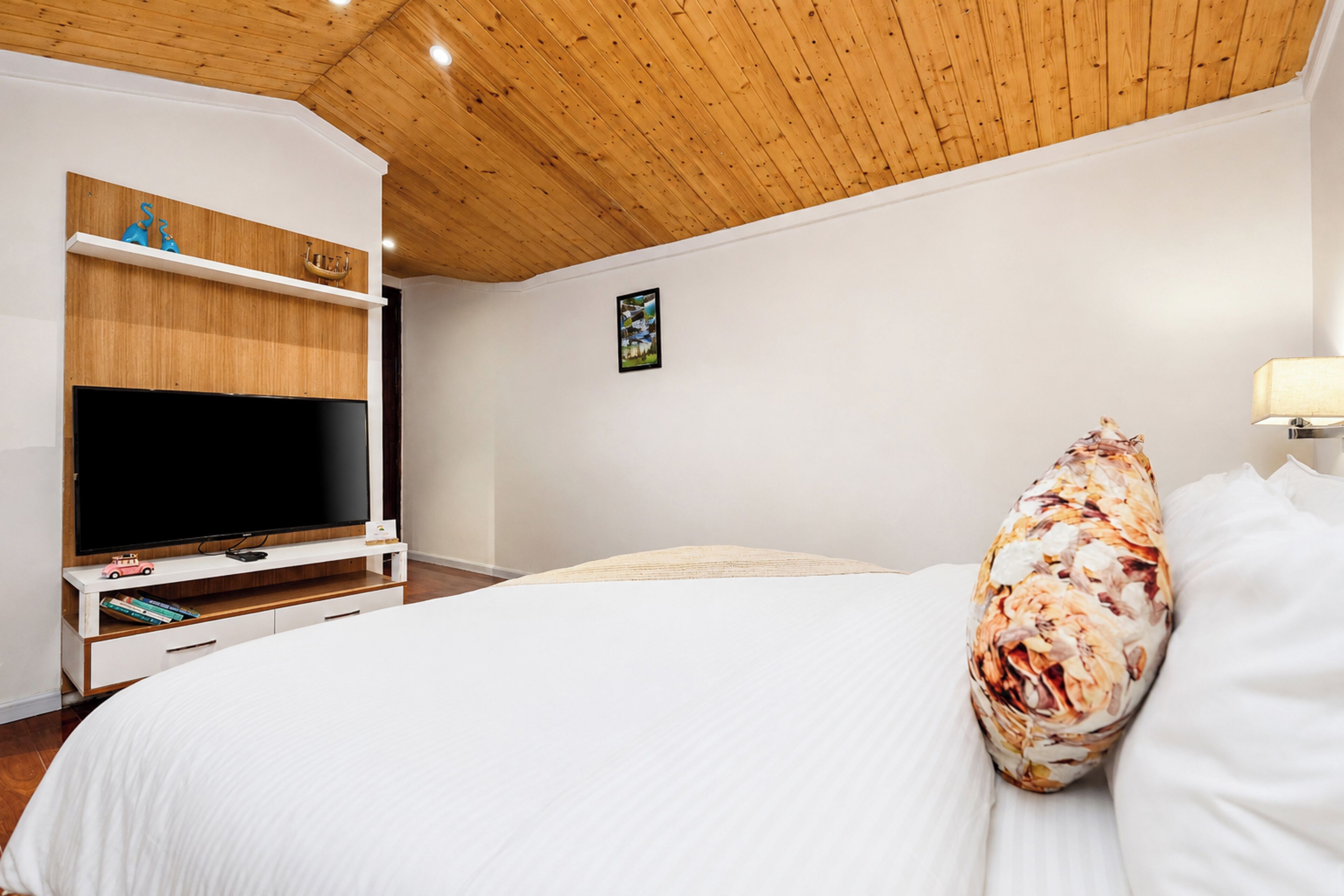 A bedroom with a large bed, a TV on a wooden stand, and a ceiling with wooden beams.