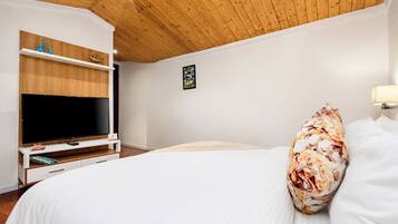 A bedroom with a large bed, a TV on a wooden stand, and a ceiling with wooden beams.