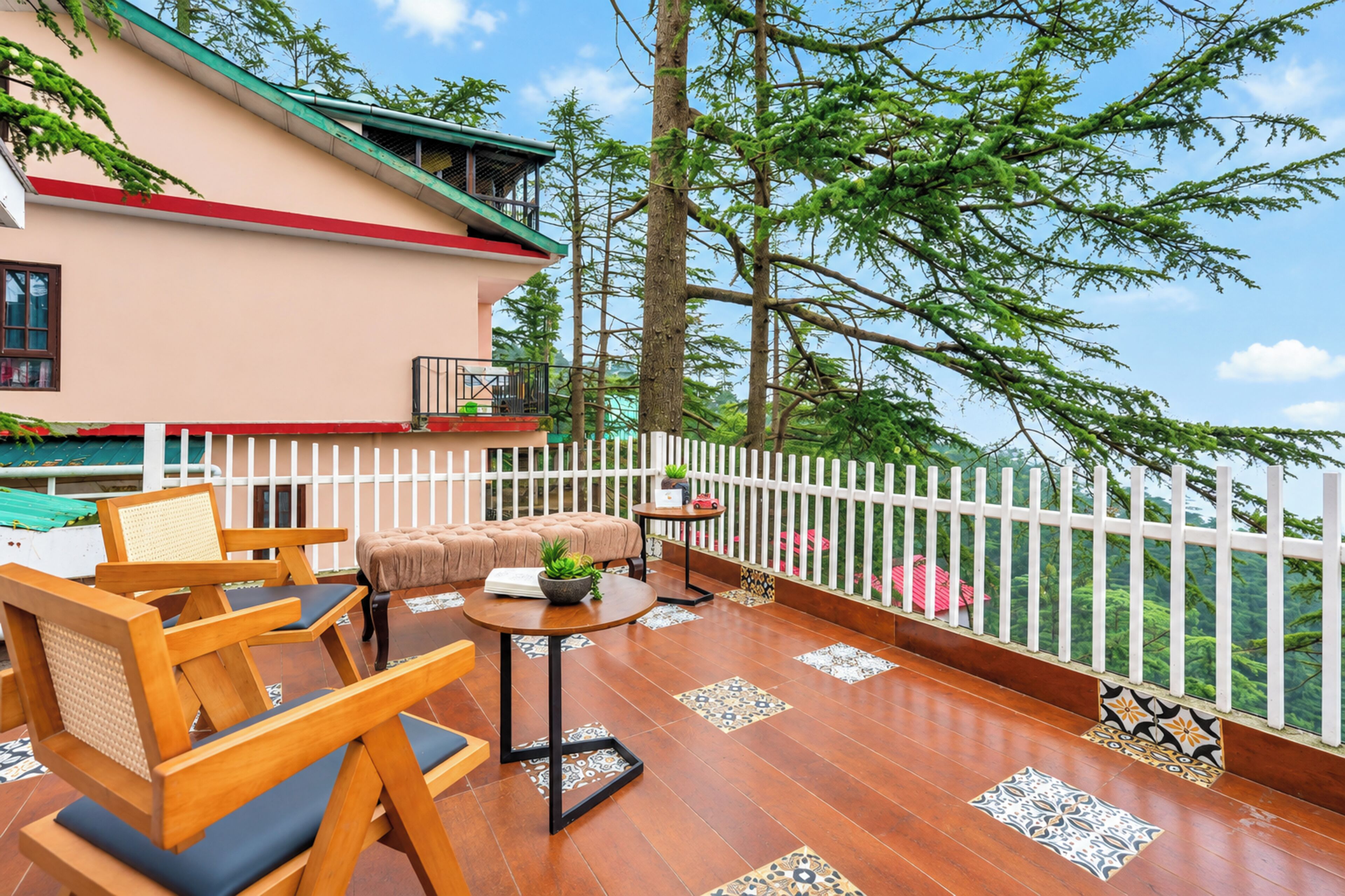 Una terraza de madera con mobiliario exterior, una valla blanca y vistas a árboles.