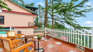 A wooden deck with outdoor furniture, a white fence, and a view of trees.